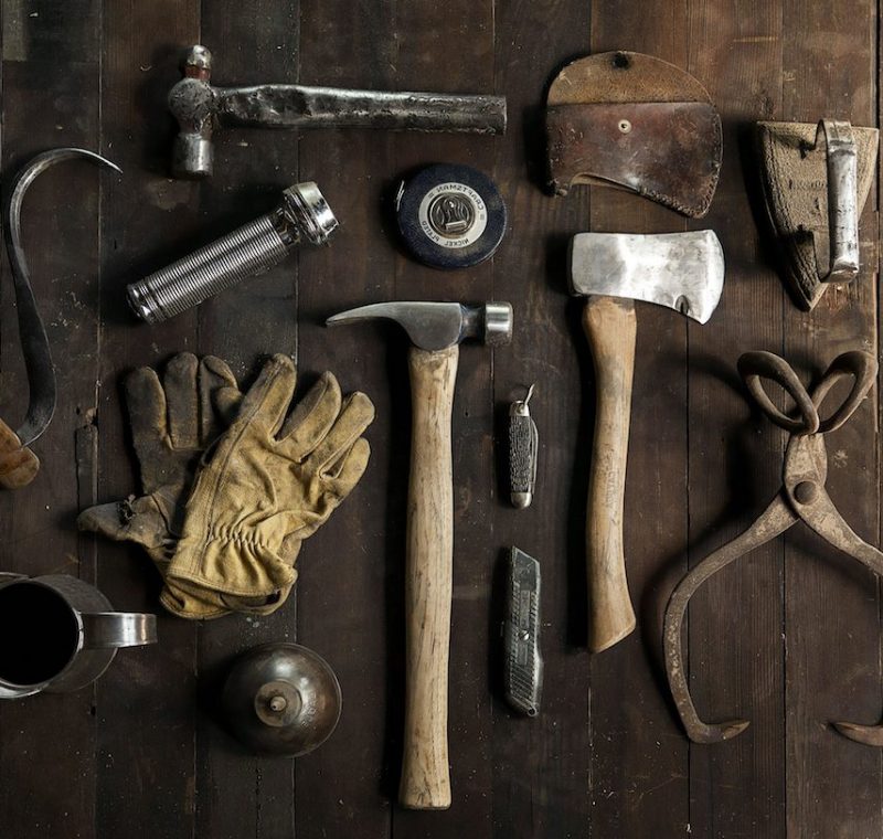 Werkzeuge wie Hammer, Handschuhe und Bügel liegen auf einen Holztisch